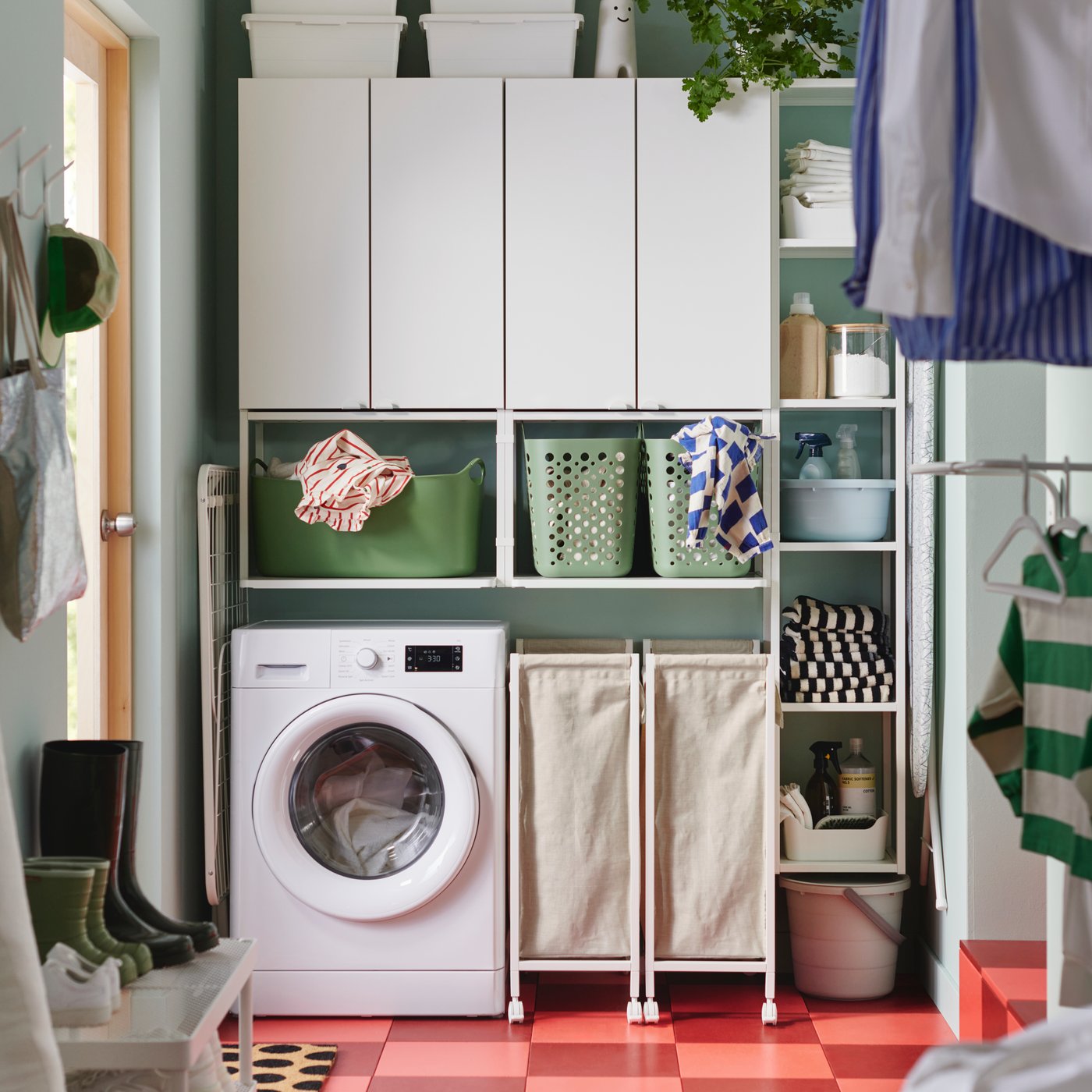 Une combinaison de rangement ENHET blanche avec des étagères murales et des armoires est placée au-dessus d'une machine à laver dans une buanderie lumineuse et moderne.