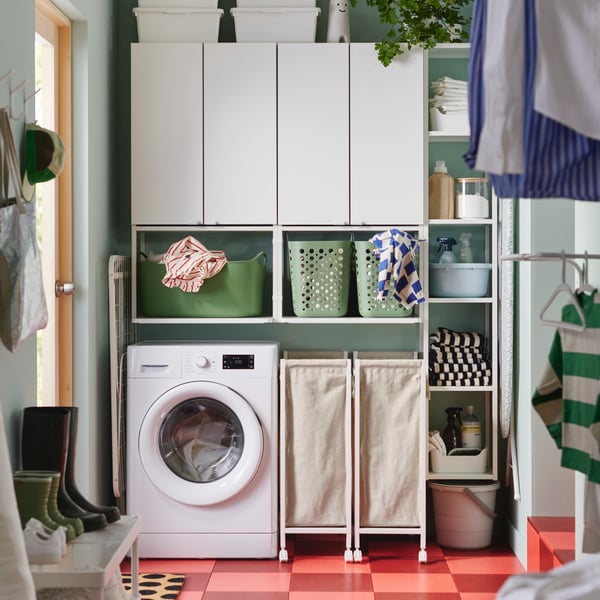 Une combinaison de rangement ENHET blanche avec une bande lumineuse LED SILVERGLANS blanche à intensité variable pour salle de bain, des étagères murales et des armoires se trouve au-dessus d'une machine à laver dans une buanderie lumineuse et moderne.