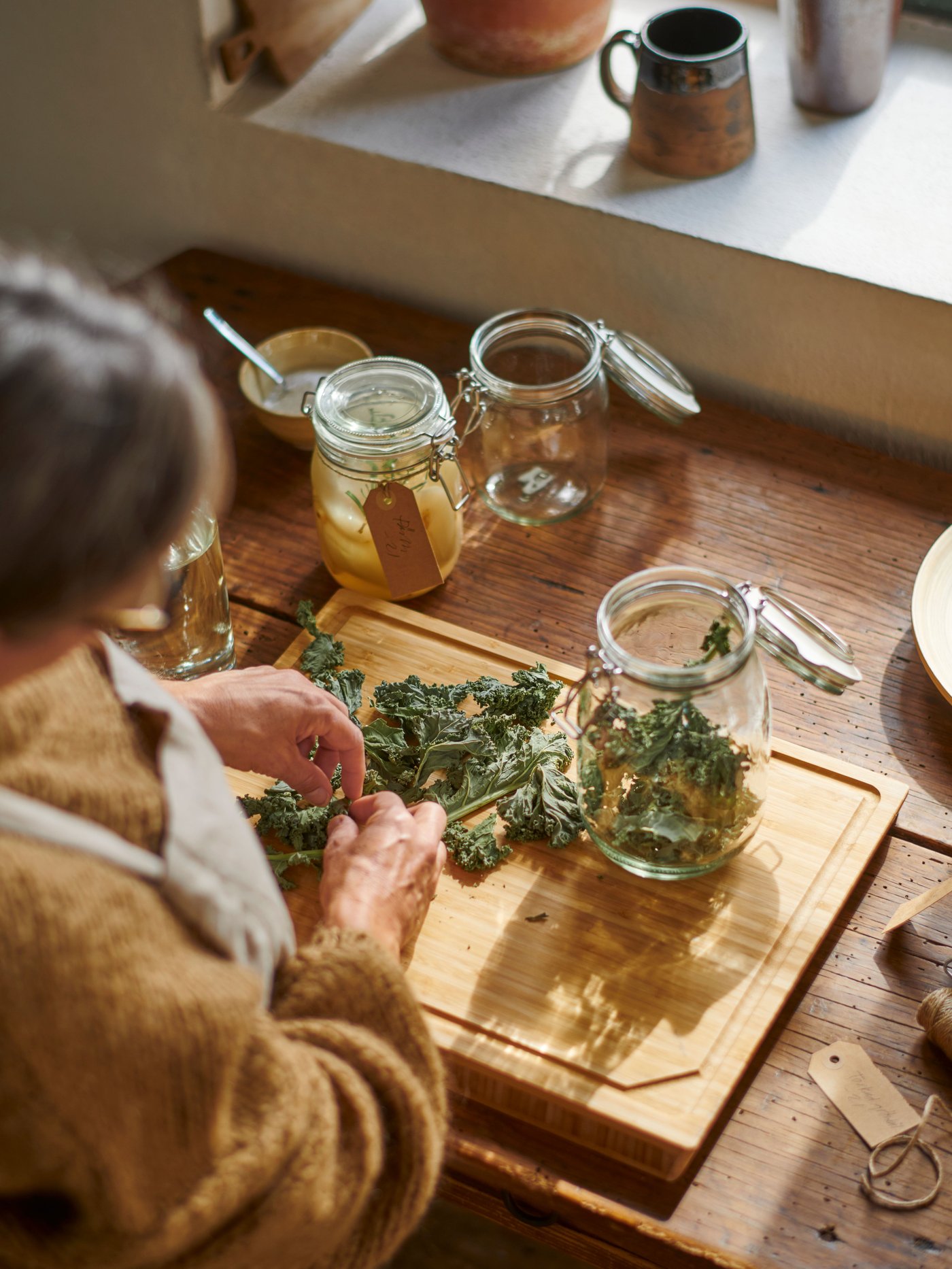 A person, wearing a mustard-coloured sweater and an apron, is picking herbs on an APTITLIG butcher’s block.