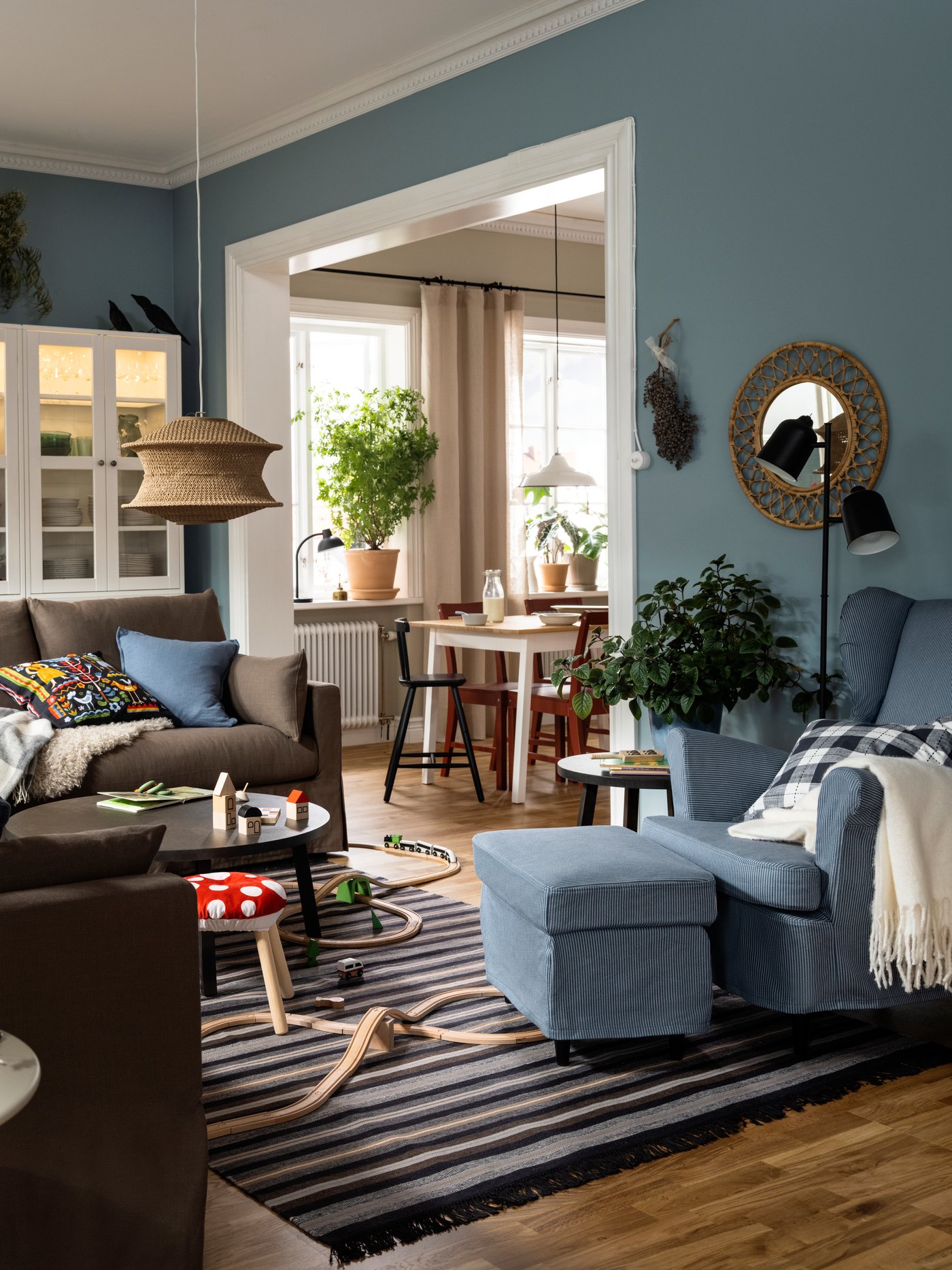 Two HYLTARP sofas stand opposite a STRANDMON wing chair and footstool on a woollen RÅVAROR rug in a flexible living room.