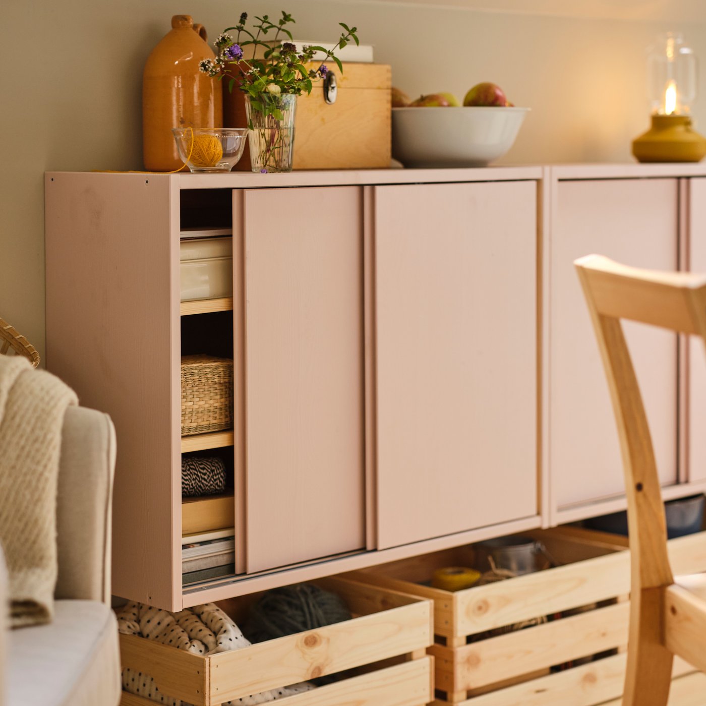 Two IVAR cabinets with sliding doors painted pink on a wall with a bowl and vases on top and KNAGGLIG boxes underneath.
