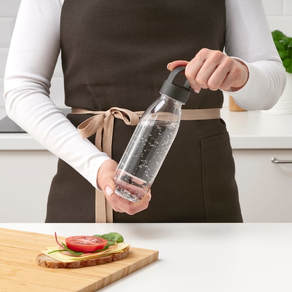 Человек держит многоразовую бутылку для воды на кухне.				