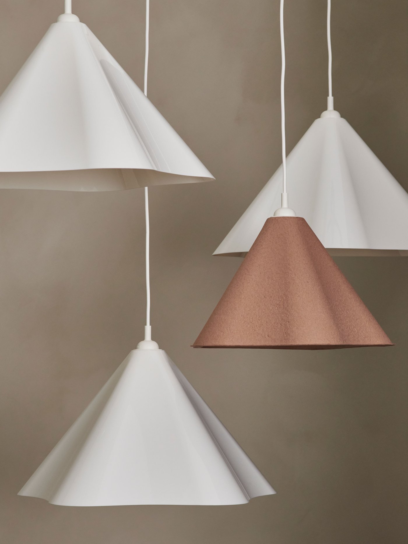 Flera ZEBRASÄV lampskärmar i vitt och en i brunrosa hänger i grupp mot en neutral bakgrund.