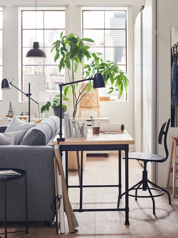 KULLABERG swivel chair and a desk, with a work/wall lamp on top, placed at the back of a grey sofa.