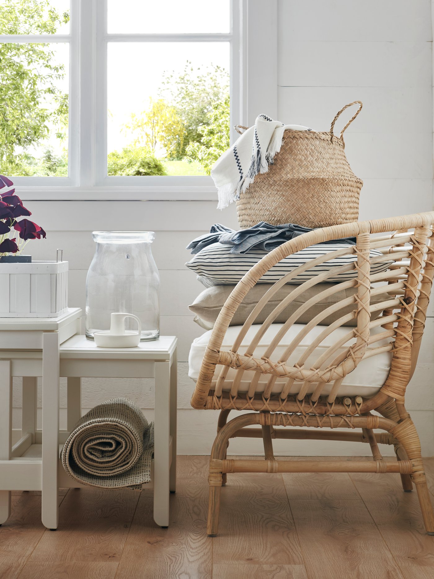 Salón con sillón, dos mesas blancas, un cesto, un florero, un candelabro, una colcha, fundas de cojín, cojines y artículos decorativos.