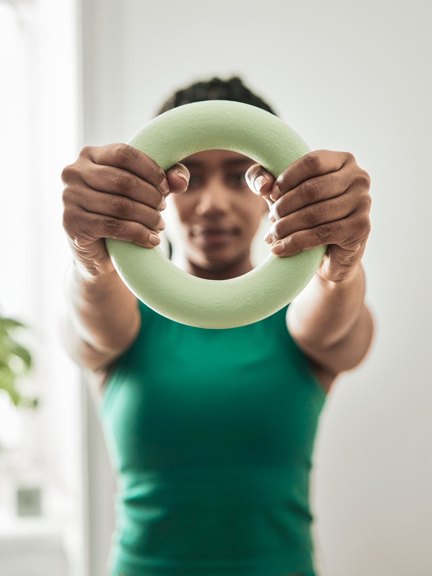 A closeup image of a girl wearing a green workout top, holding a round DAJLIEN training weight in front of her.