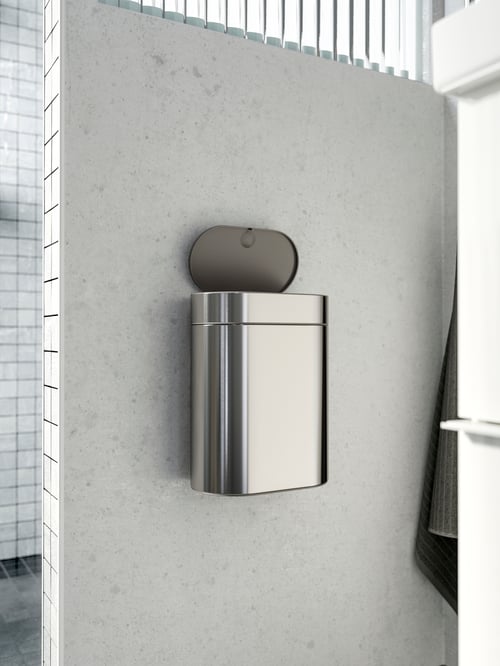 Bathroom setting featuring a shot of an open touch top bin which is mounted on a grey wall, with a tiled wall in the back.