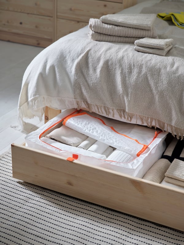 An extended drawer of a GLAMBERGET extendable bed with storage in pine with a PÄRKLA underbed storage bag in it.