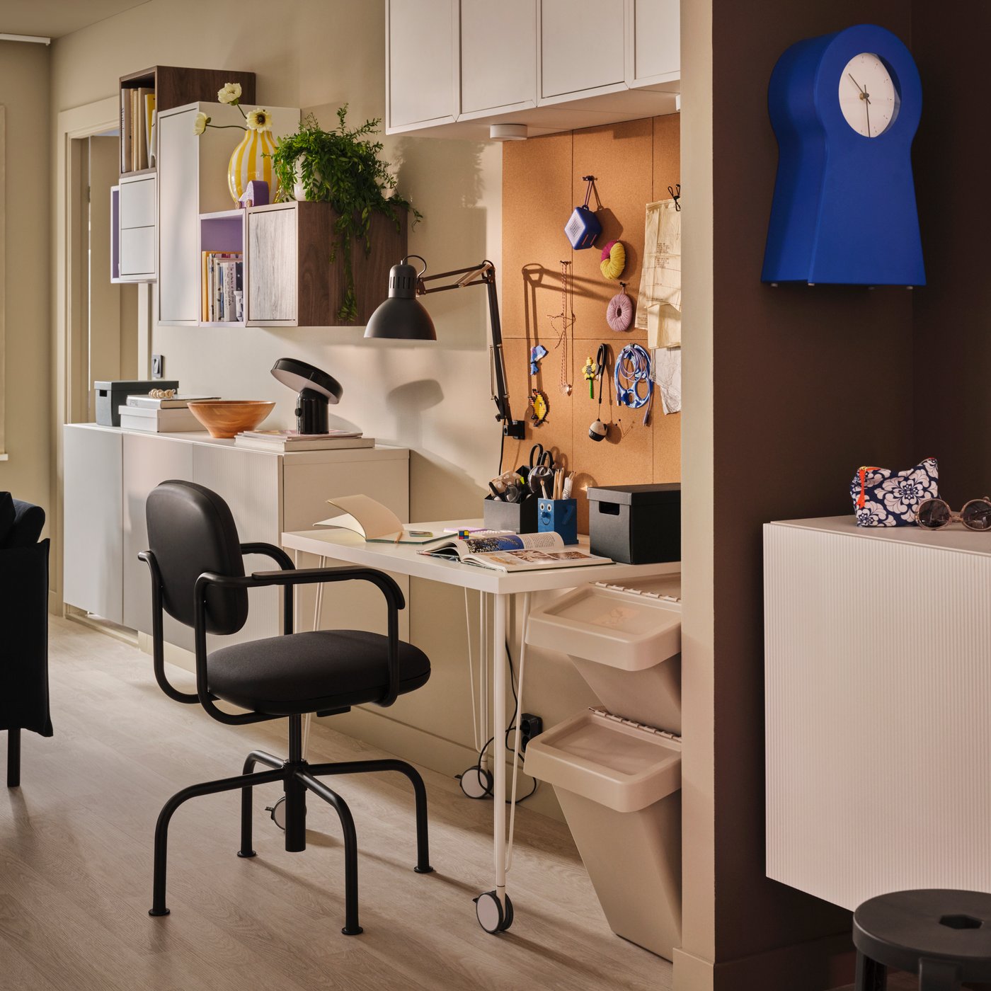 A living room with a LINNMON-KRILLE desk beneath FLÖNSA memo boards and clusters of wall-mounted EKET and BESTÅ cabinets.