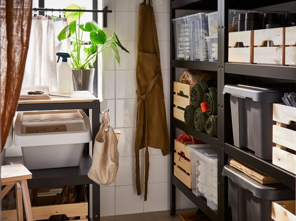 A tiled storage room with two black BROR shelving units. All shelves are filled with large wooden and plastic storage boxes.