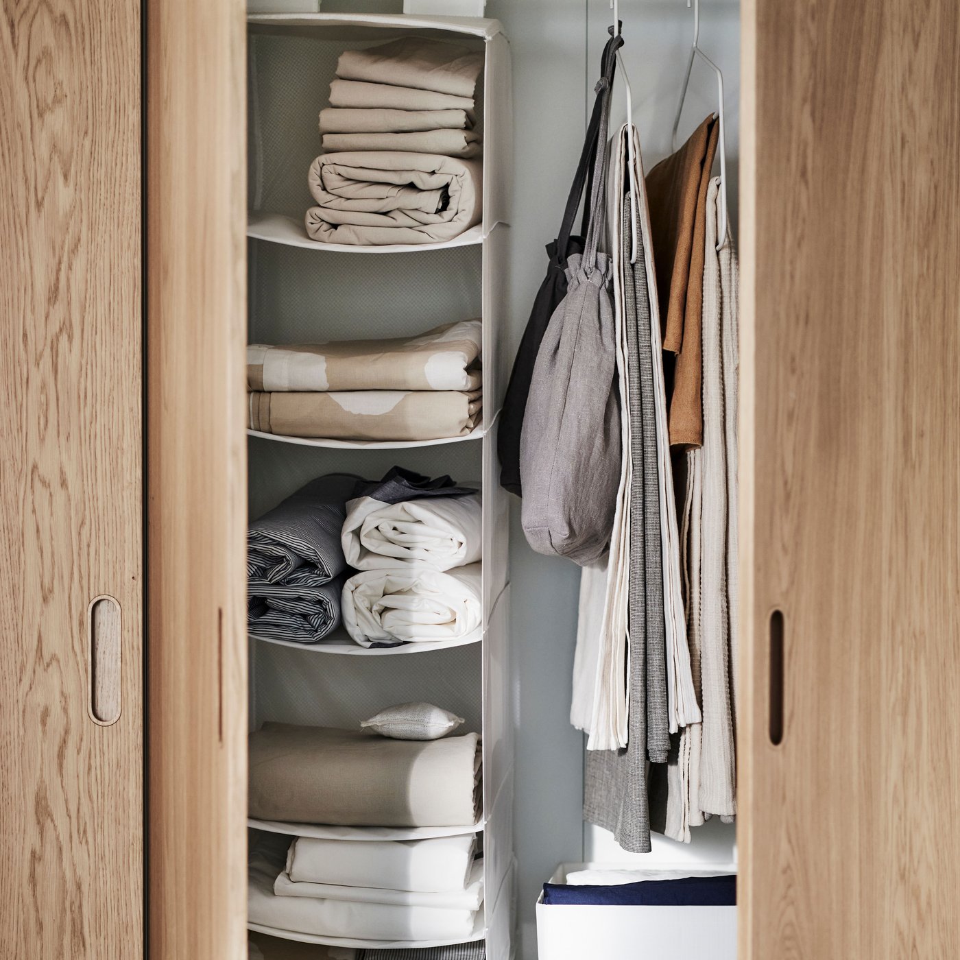 Et PAX/TONSTAD garderobeskab i hvidt/egetræsfiner med åbne døre, hvor man kan se hvid SKUBB opbevaring med 6 rum.