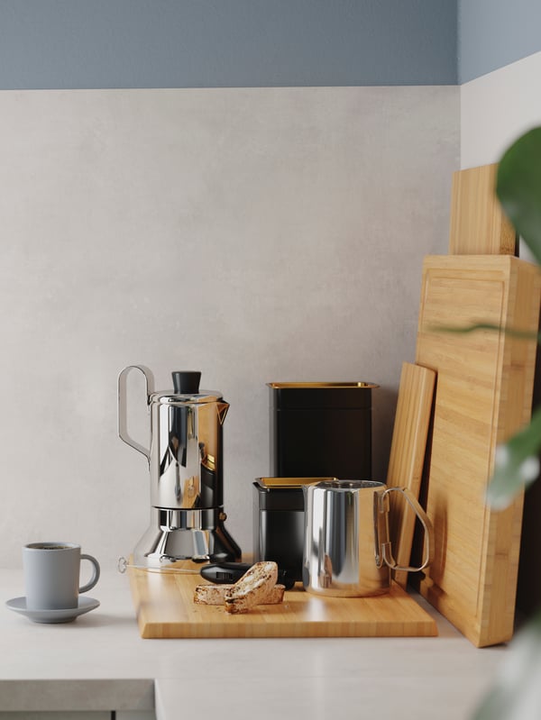 A kitchen worktop corner with chopping boards in bamboo, an espresso maker in stainless steel and two black coffee tins.