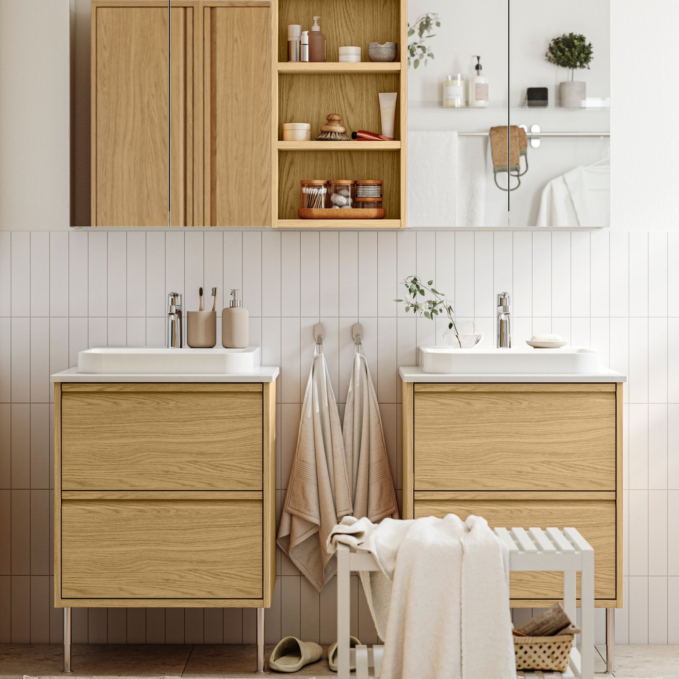 A bright bathroom has ÄNGSJÖN bathroom furniture in oak effect, including two wash-stands with drawers and mirror cabinets.