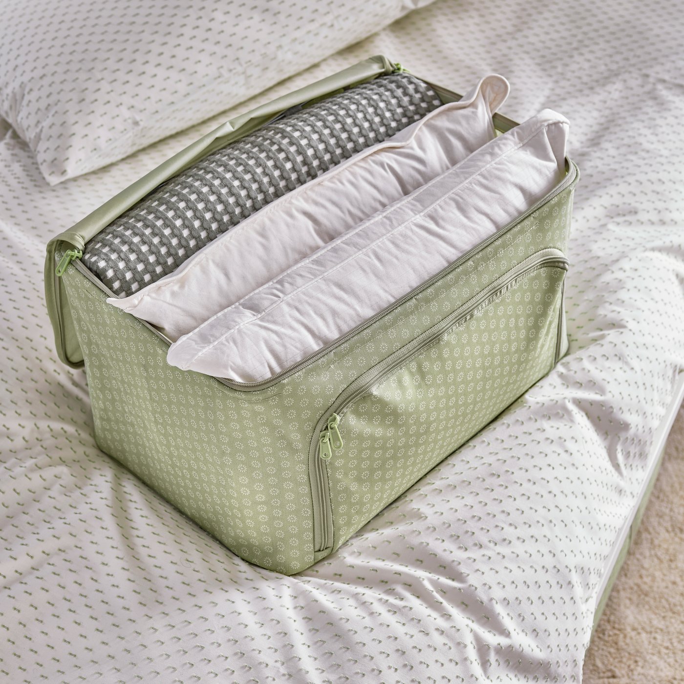Un contenitore per indumenti HEMMAFIXARE verde appoggiato su un letto