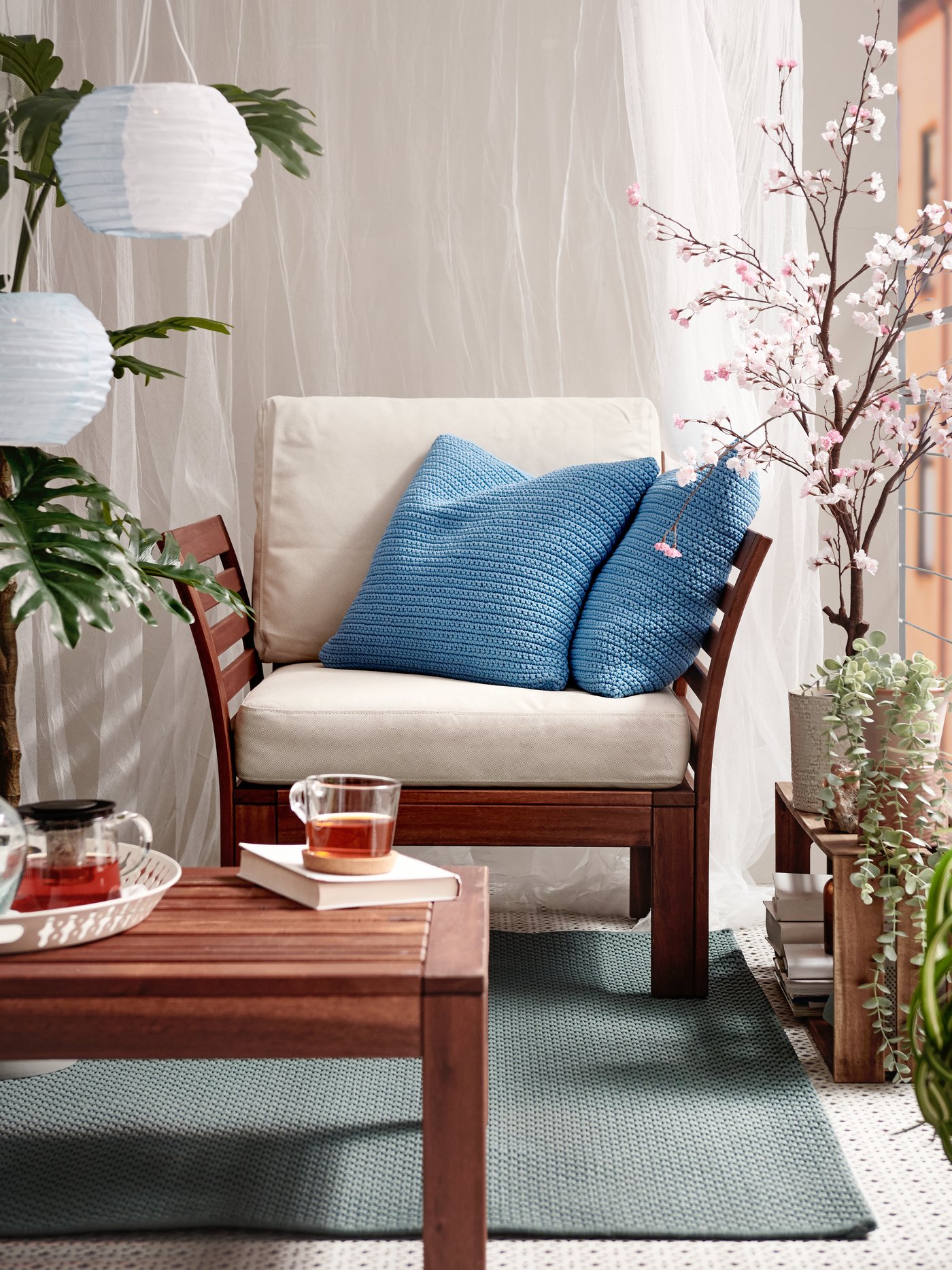 Un sillón de madera con dos cojines que tienen fundas azules SÖTHOLMEN. Hay plantas a ambos lados y una mesa delante.