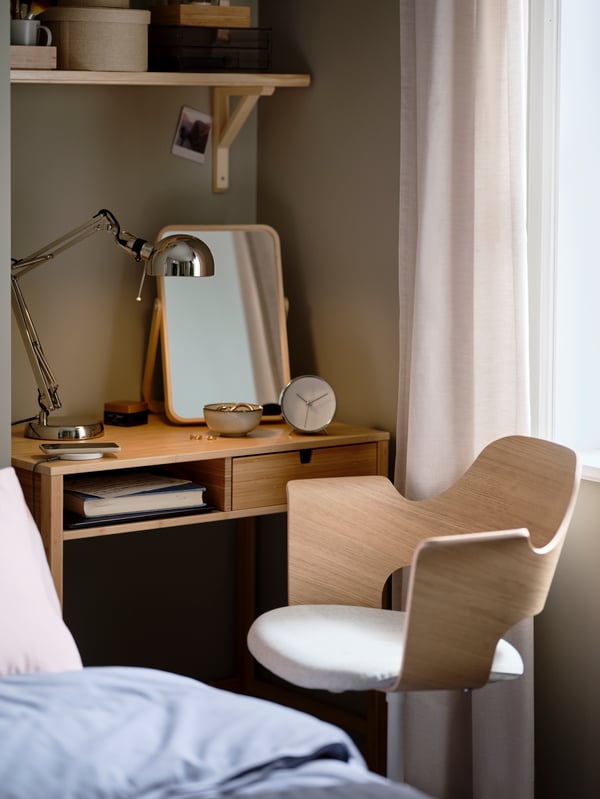 A bedroom with a FJÄLLBERGET conference chair with castors standing by a NORDKISA dressing table with a lamp and mirror on.