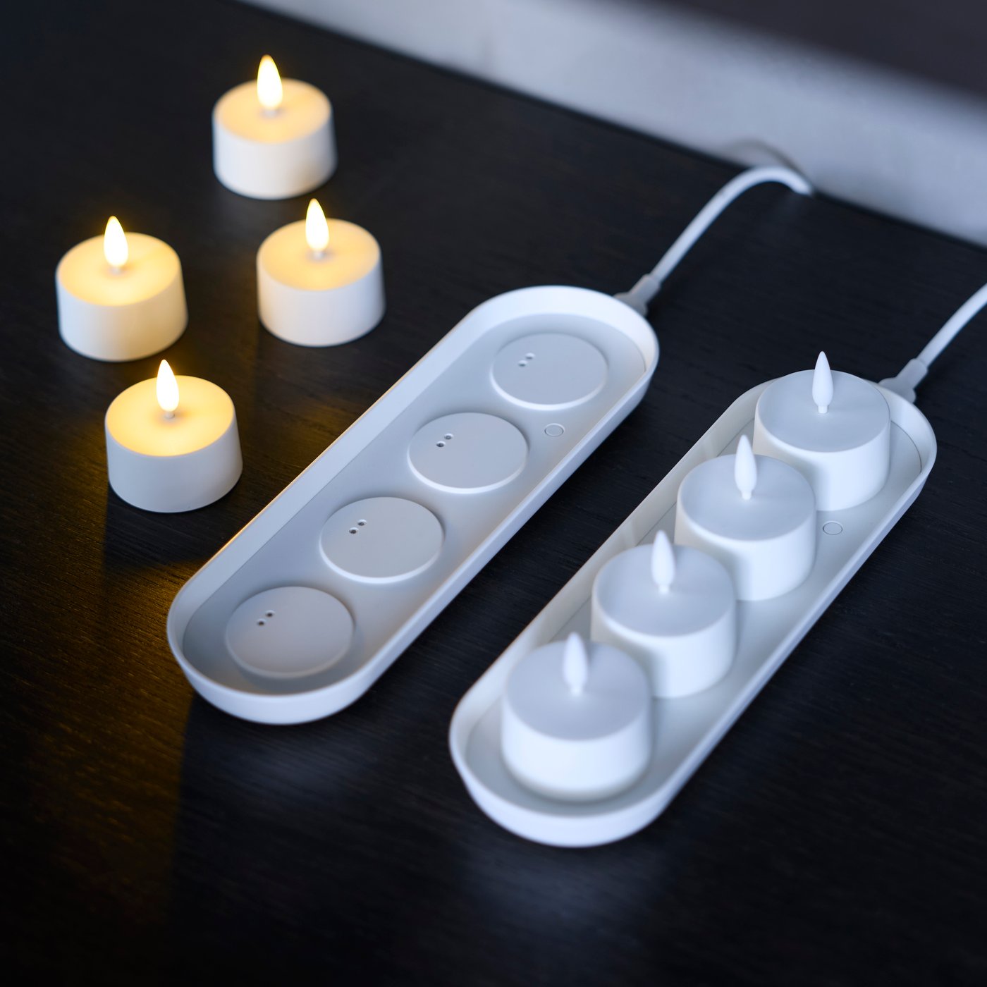 Two sets of a chargeable tray with SKATGÅS LED tealights on a black surface.
