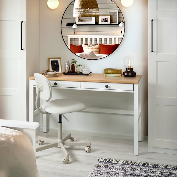 White desk being used as a dressing table with a large round mirror above and lights on either side