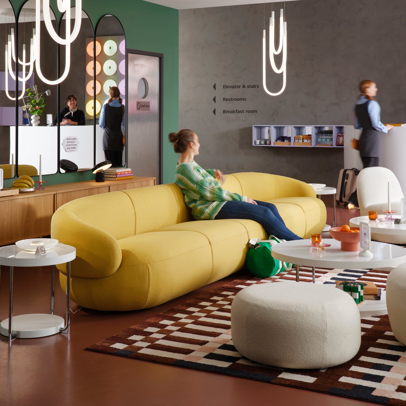 A multicolour/check patterned MARKBLÅMME low pile rug is in modern hotel lounge that has guests on the sofa and at reception.