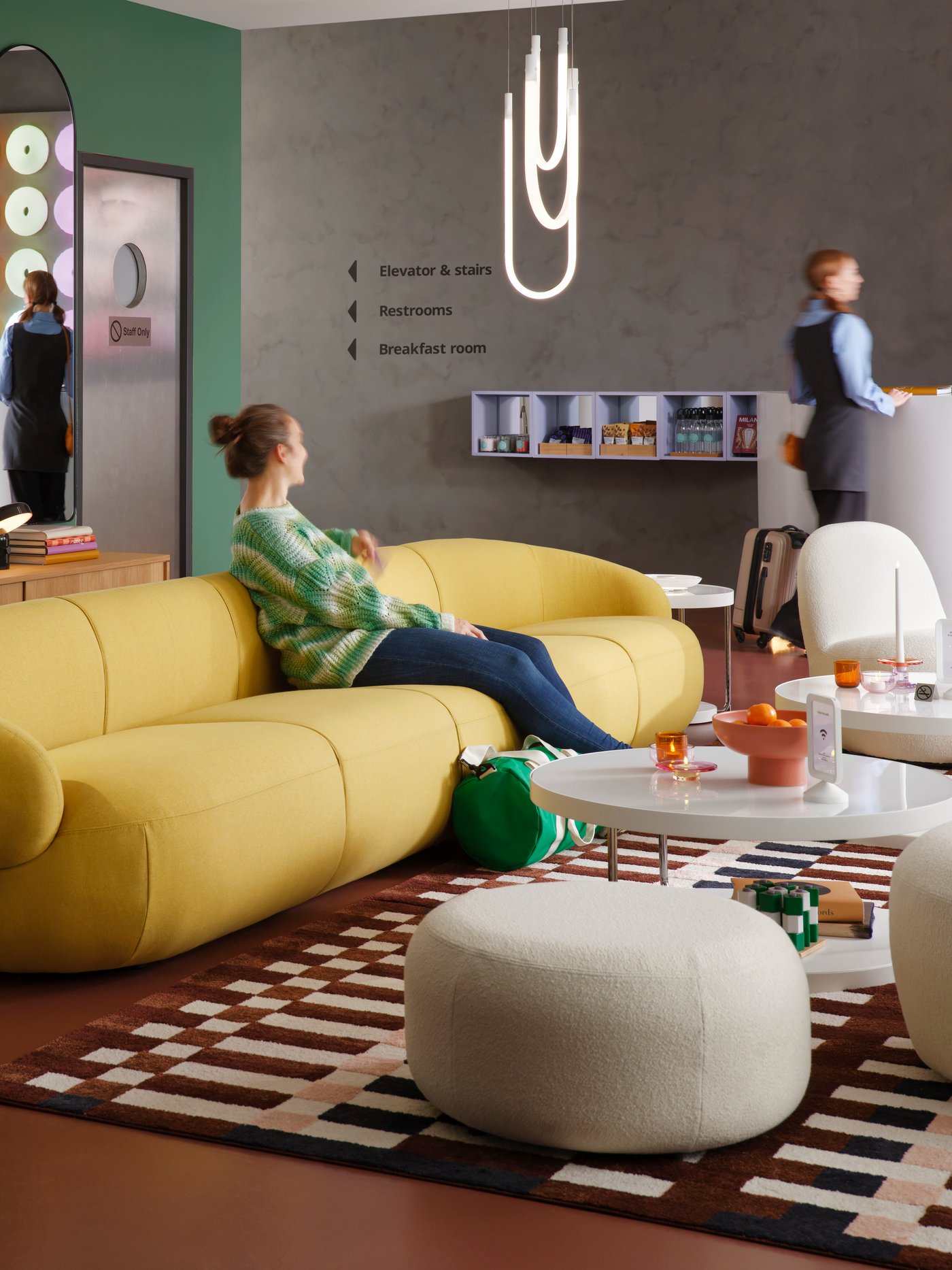 A multicolour/check patterned MARKBLÅMME low pile rug is in modern hotel lounge that has guests on the sofa and at reception.