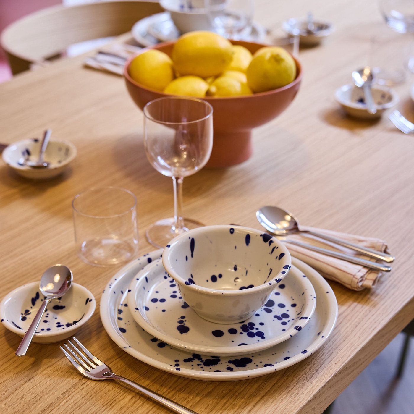 Houten eettafel met servies en bestek, kom met citroenen centraal, glazen en lepeltjes netjes geschikt, sfeervolle tafeldekking.