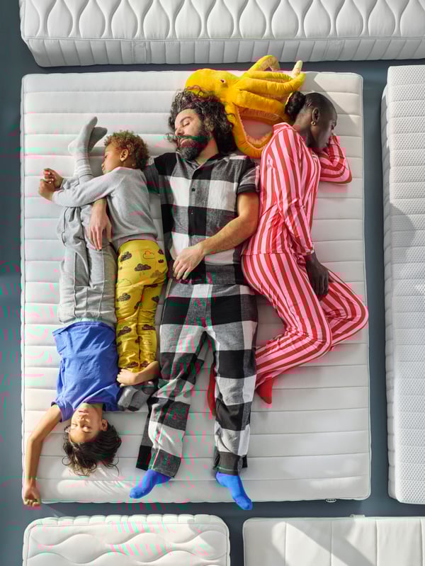 A close up of a family of four, wearing pyjamas, testing the comfort of an IKEA VALEGÅG mattress.