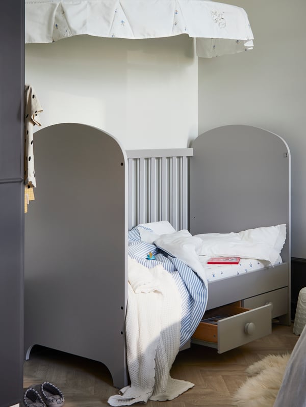 Un lit d’enfant GONATT avec un côté enlevé et un tiroir ouvert est placé dans un coin, sous un ciel de lit RÖDHAKE.