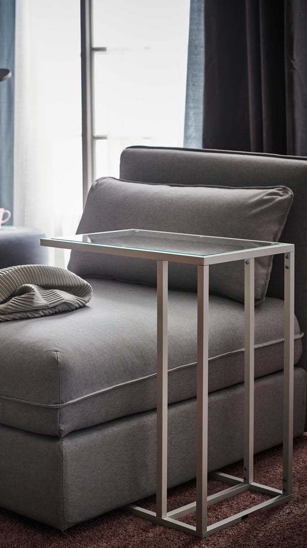 A woman is on her phone laying on the sofa. In front of her is a BJÖRKÅSEN laptop stand and TROTTEN storage unit on castors.