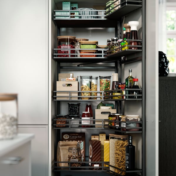 A pantry with UTRUSTA pull-out larder, filled with jars, bottles, pasta, sauces, and wooden boxes on the shelves.