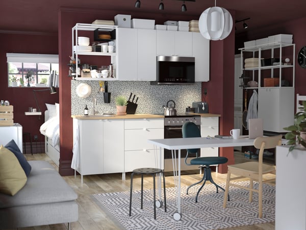 Una combinación de cocina ENHET blanca a lo largo de una pared en un departamento tipo estudio con un escritorio al frente y una cama detrás de la pared.