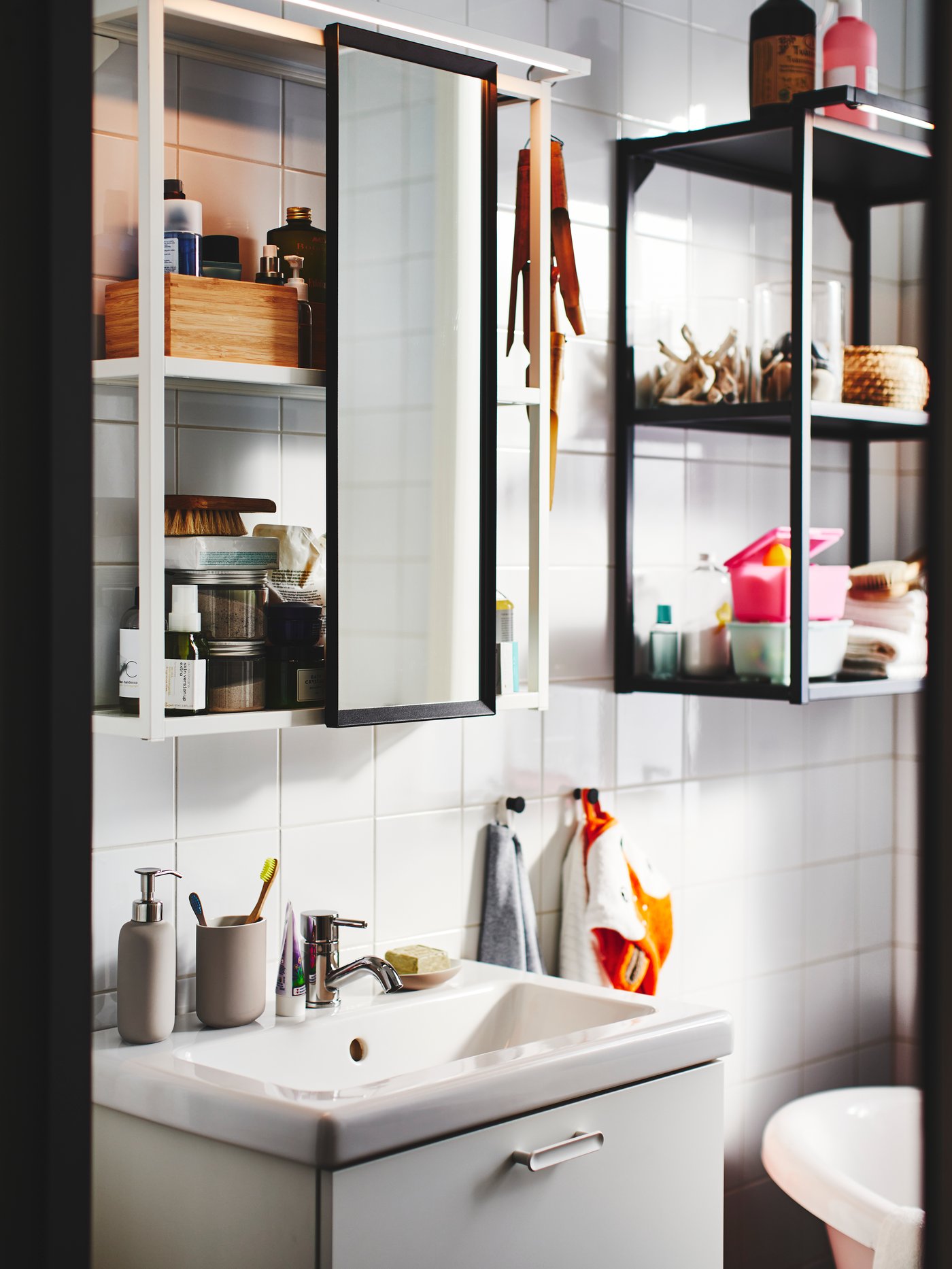 Cuarto de baño con un armario con espejo blanco de acero, un lavabo con 2 cajones y un marco de pared negro con estantes.