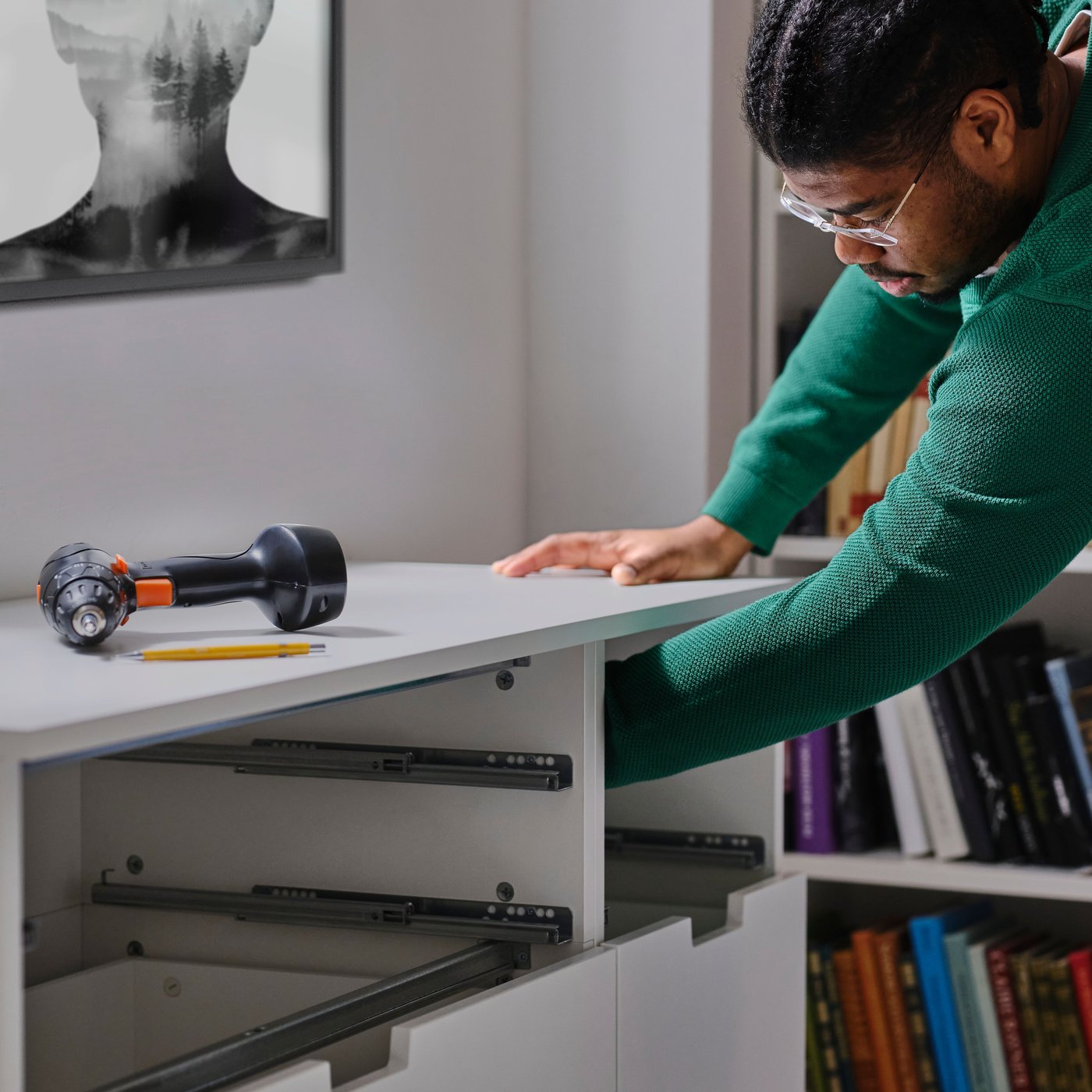 Homme portant un chandail vert et assemblant une commode en veillant à la fixer au mur pour éviter tout risque de basculement.