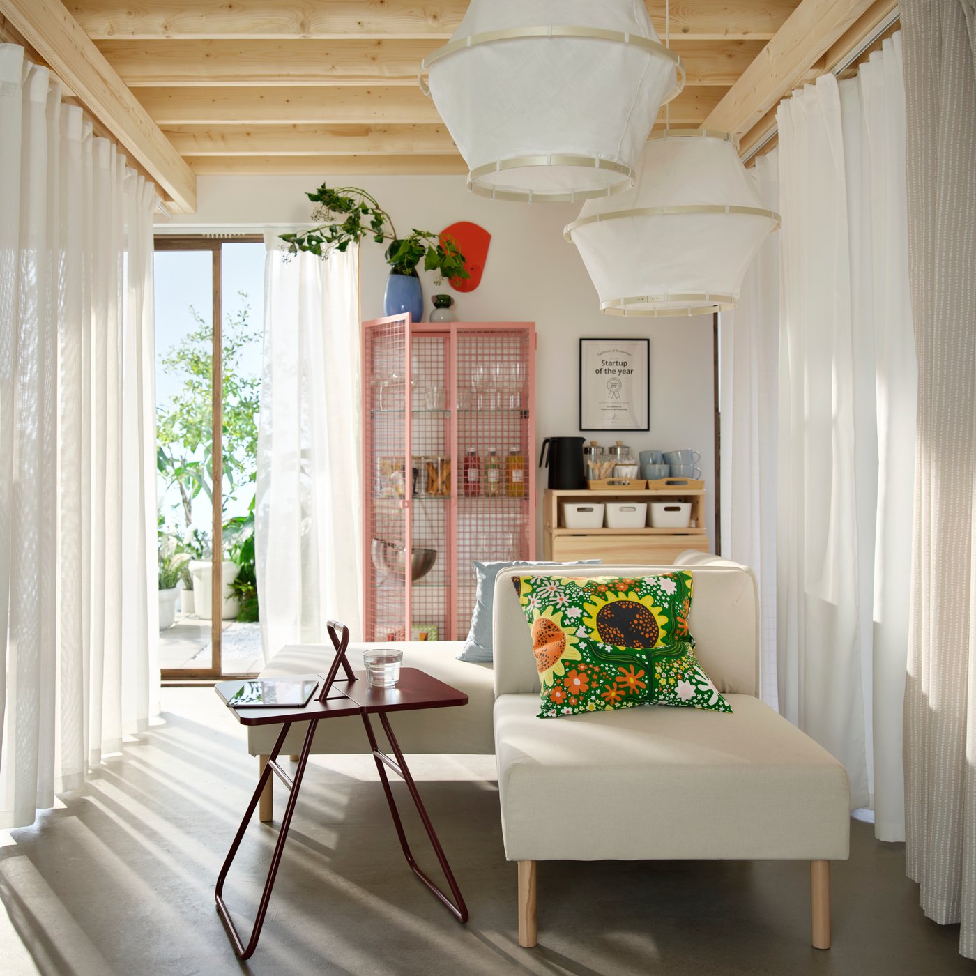 A lobby /lounge area with coffee table, white sofas and printed cushion. Behind are a glass cabinet and pine drop-leaf table.