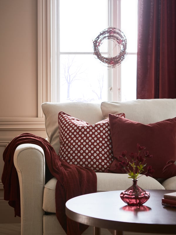 A GRÖNLID sofa with cushions in a red/brown SANELA cover and a SNÖBRACKA cover stands in front of a window.