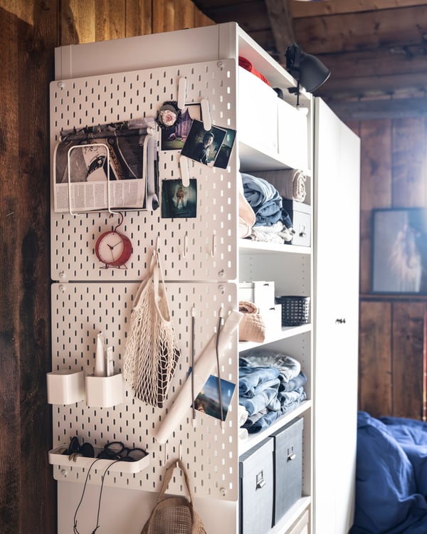 2 SKÅDIS Lochplatten sind untereinander hängend, seitlich an einem Schrank befestigt. Daran sind Ablagen und Klemmen befestigt die Kopfhörern, Fotos und anderen Dingen Platz bieten.  
