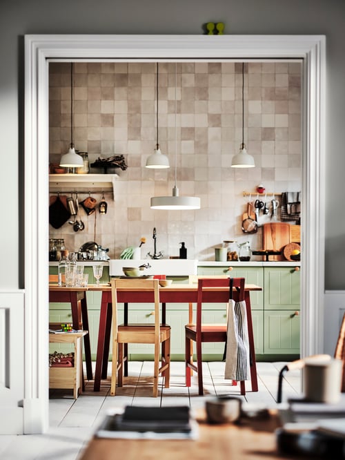 Kitchen area with green drawer fronts attached to base cabinets, pendant lamps, a table with multiple chairs, and a bench.