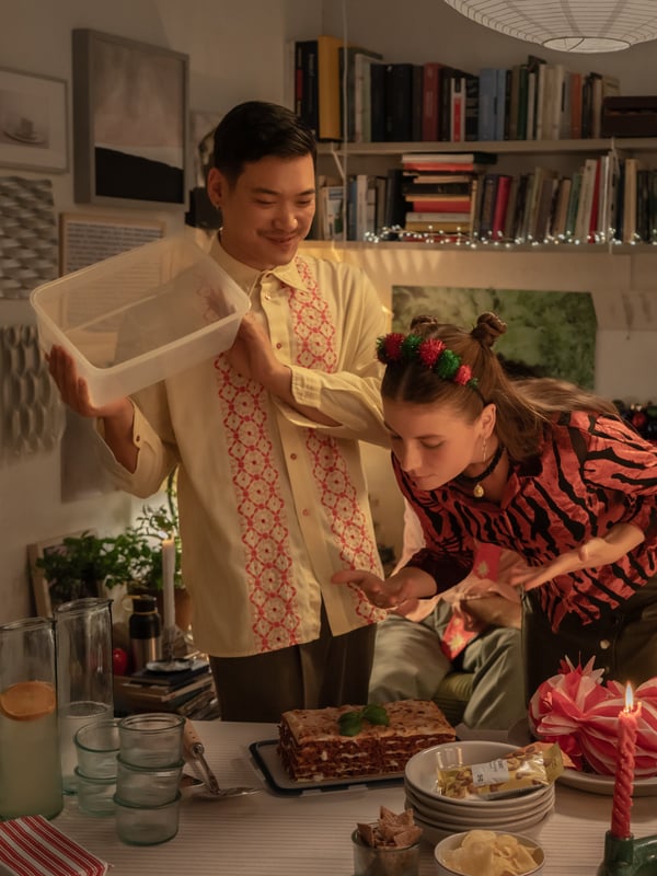 Un ragazzo e una ragazza sorridono mentre si preparano a conservare una lasagna appena cotta in un contenitore per alimenti IKEA 365+ dopo una cena in compagnia.