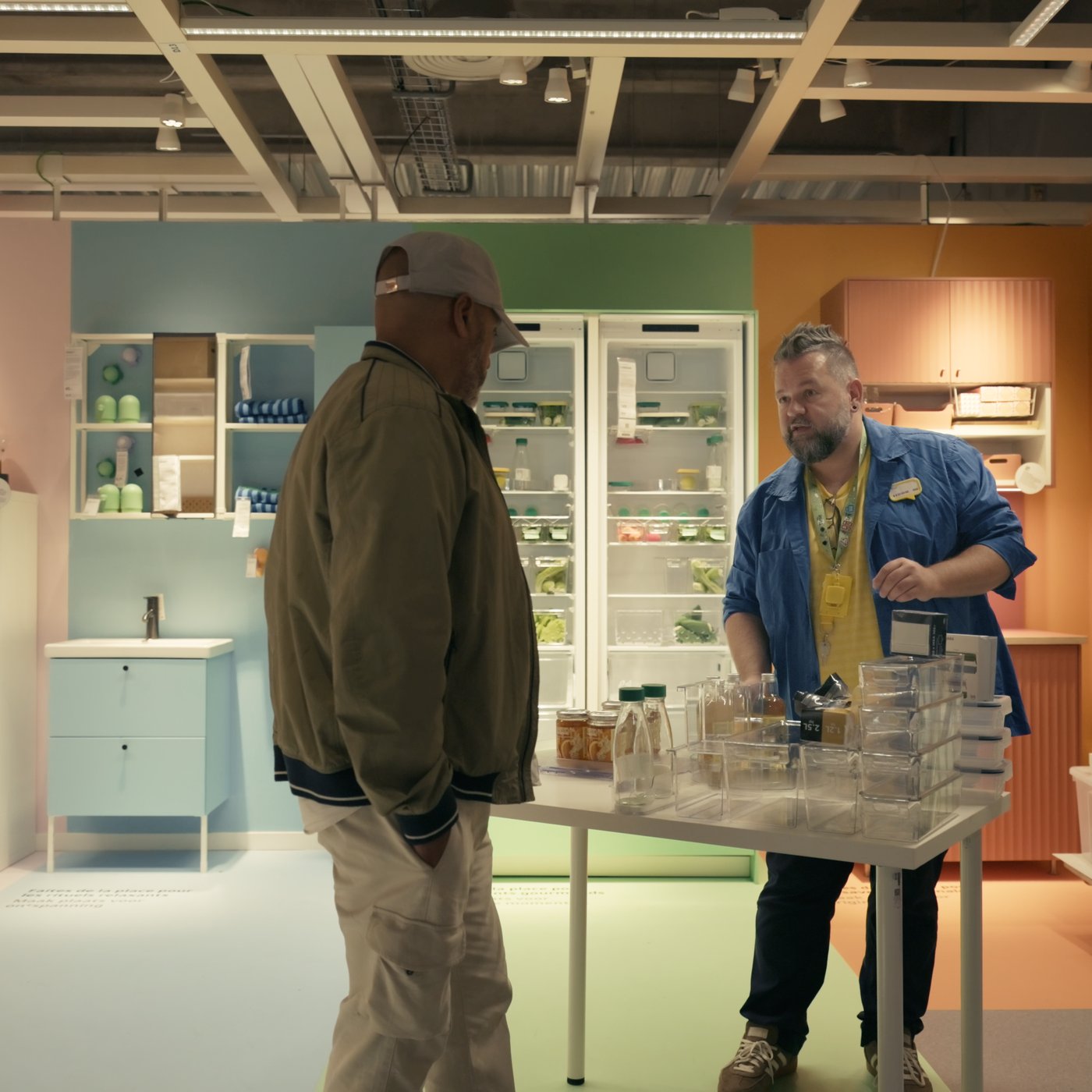 Bezoeker bekijkt voedselbewaarproducten terwijl een IKEA-medewerker uitleg geeft aan een demonstratietafel in de winkel.
