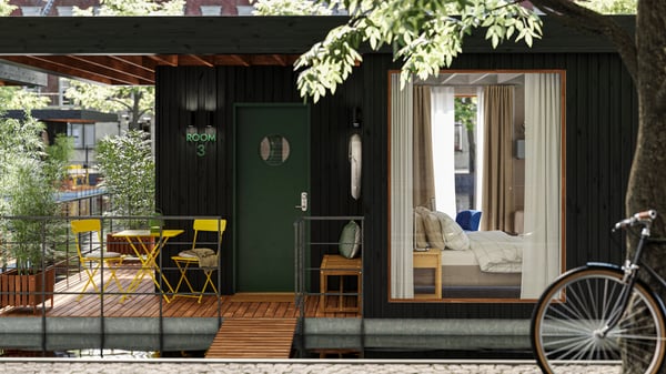 The deck of a small houseboat hotel floating on water in an urban context. One room with a bed can be seen through a window.
