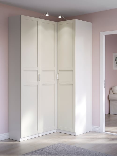 A white PAX corner wardrobe with Flisberget light beige panelled doors stands closed in a pink room. It is beside a doorway.