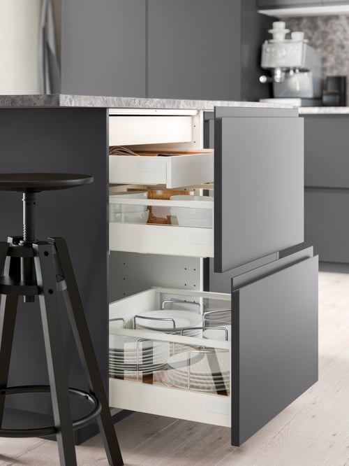 Kitchen with base cabinet with two fronts and two drawers, plates, serving bowls, cutlery, bar stool, espresso machine.