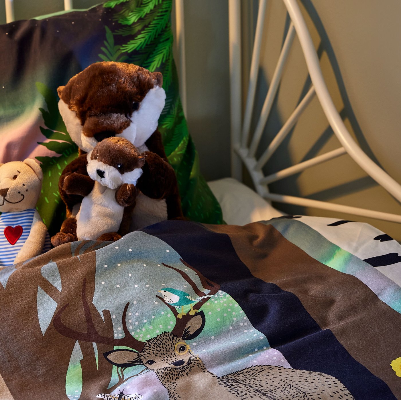 Cantó d'un llit infantil amb roba de llit SKOGSDUVA, i llúdries de peluix i el peluix FABLER BJÖRN arraulits a dins.