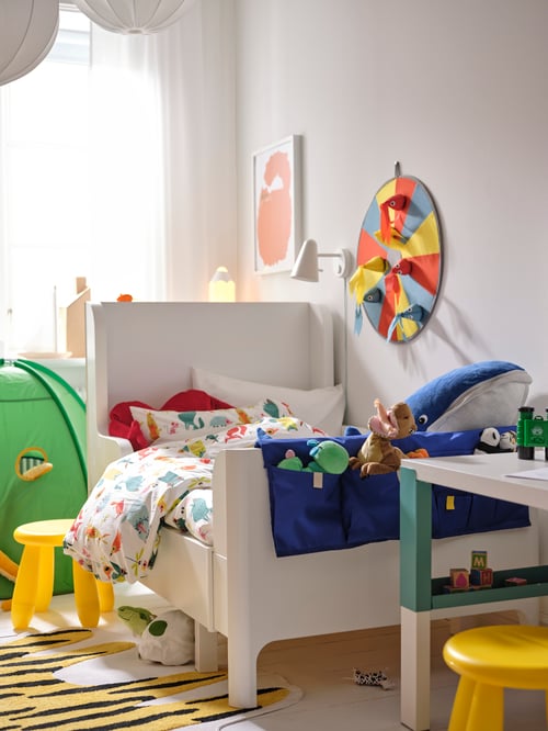 Cameră pentru bebeluși și copii cu un pat extensibil BUSUNGE alb, o veioză PELARBOJ LED și un buzunar pentru pat MÖJLIGHET albastru.