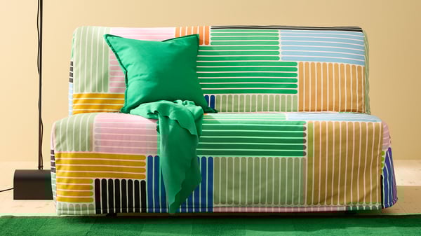 Färgglad LYCKSELE bäddsoffa med randigt överdrag och grön filt i en lekfull miljö.