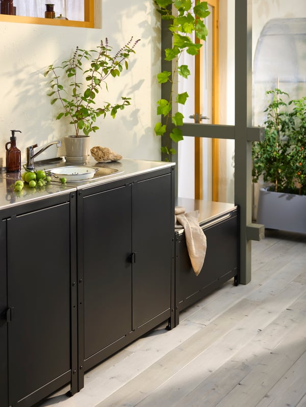A sunny veranda with a GRILLSKÄR outdoor kitchen sink unit and other, complementing units, all in black, stainless steel.