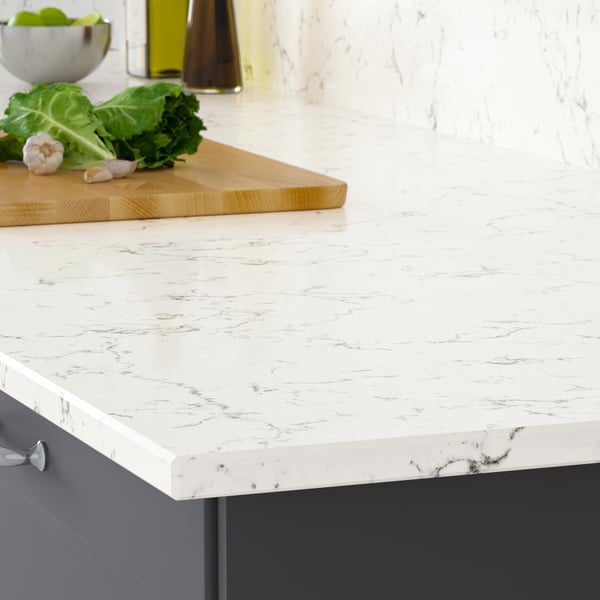 The corner of a LOCKEBO light gray white marble effect countertop on a white kitchen cabinet with a stainless steel pot on a trivet.