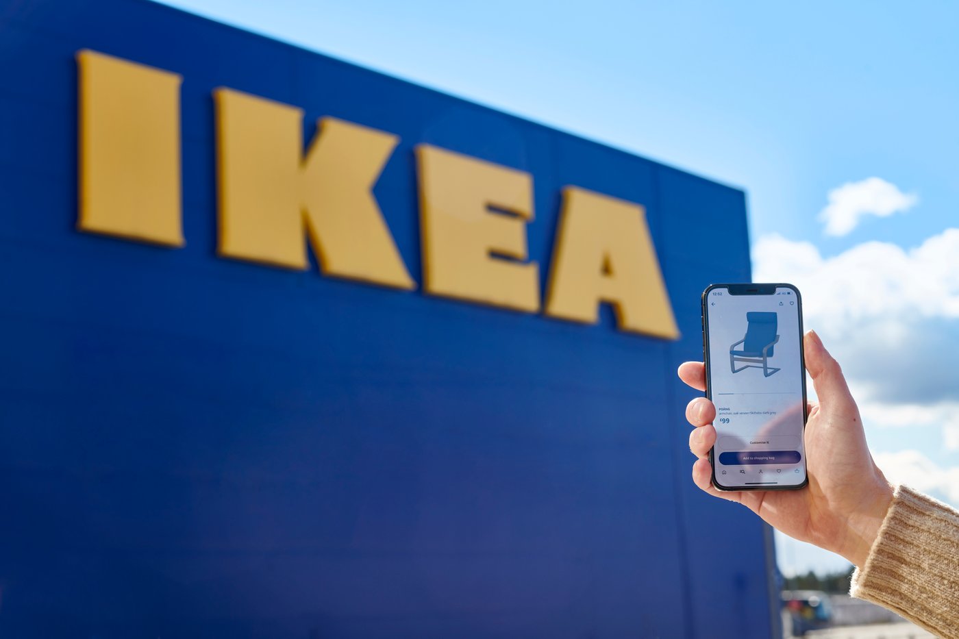 Hand holding up a mobile phone featuring an IKEA product, with IKEA store in the background