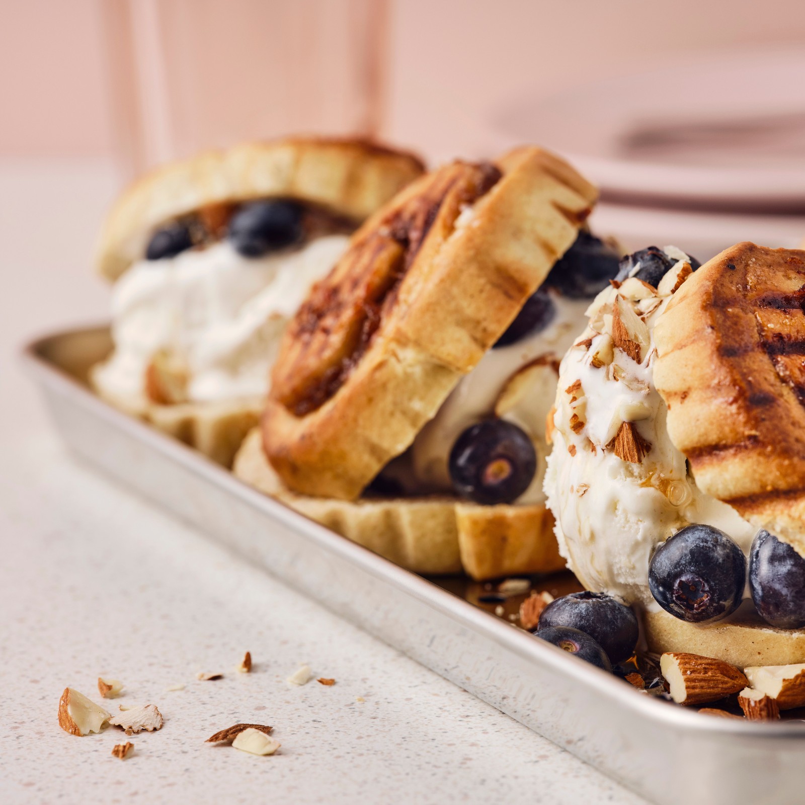 Tri prepečena KAFFEREP peciva s cimetom, sladoled, borovnice, javorov sirup i seckani bademi na metalnom poslužavniku.