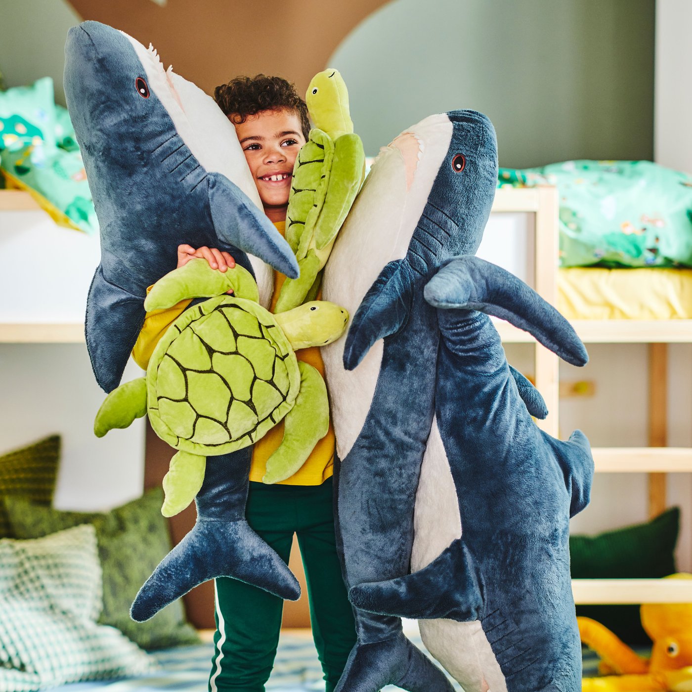 A child hugs BLÅHAJ soft toy sharks and BLÅVINGAD soft toy turtles with 100% polyester filling hollow fibre (100% recycled).