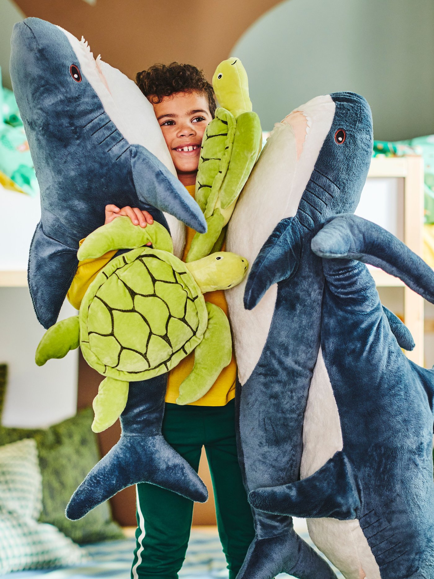 A child hugs BLÅHAJ soft toy sharks and BLÅVINGAD soft toy turtles with 100% polyester filling hollow fibre (100% recycled).